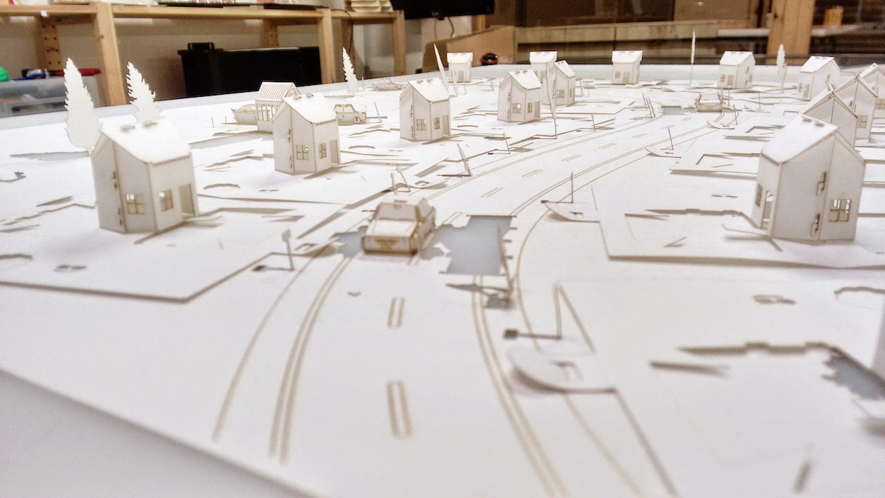 primer plano de una maqueta de cartulina blanca con un montón de casitas pequeñas y un coche.